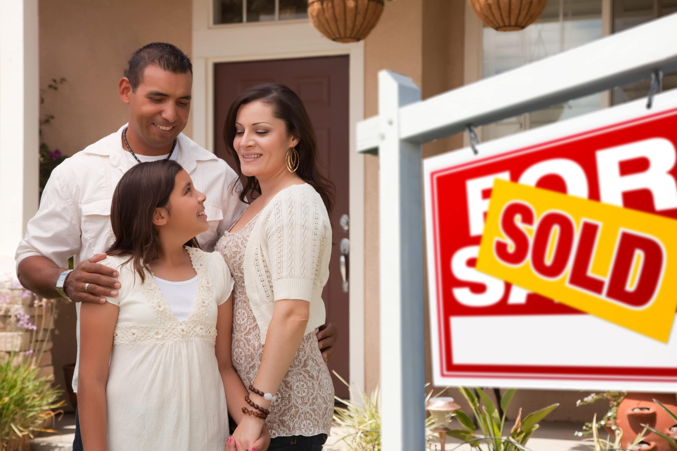 Hispanic Mother, Father and Daughter in Front of Their New Home with Sold Home For Sale Real Estate Sign